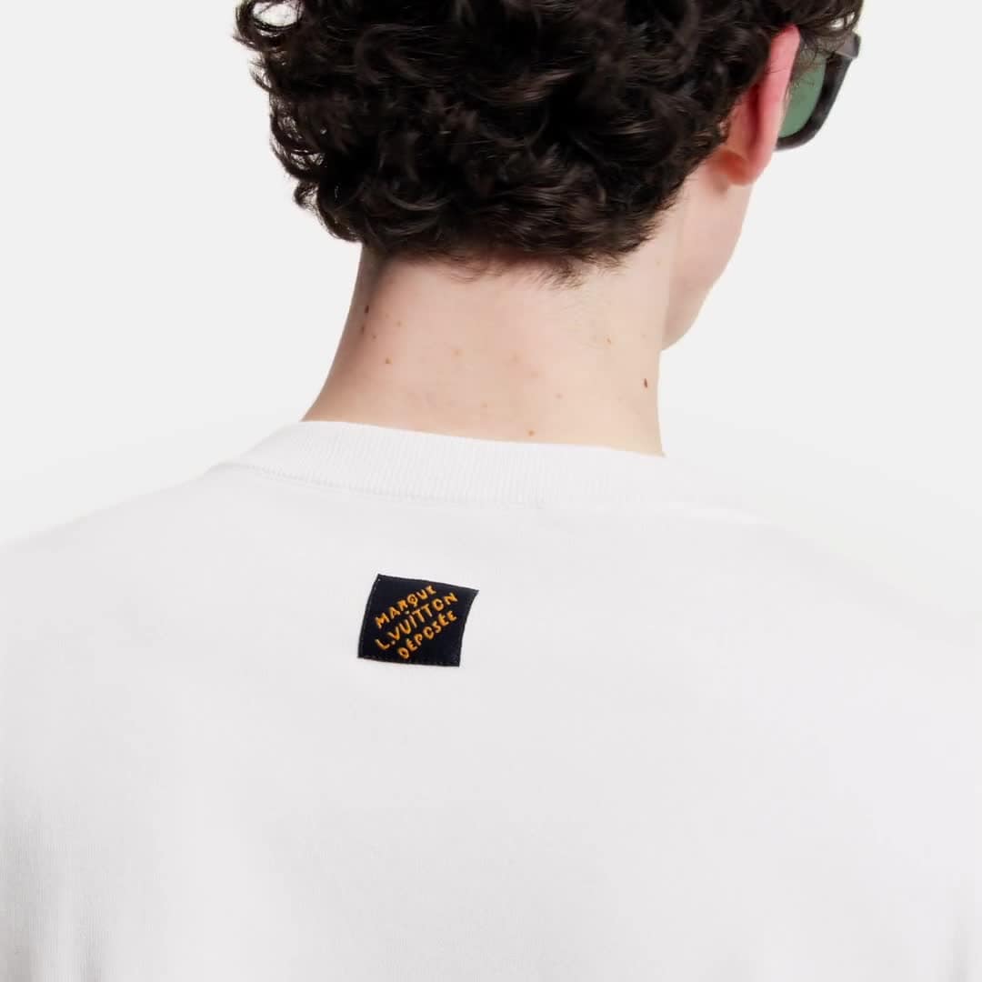 tee-shirt blanc à manches courtes, orné d'un patch bleu roi représentant les mains de Pharrell Williams formant le geste LV, est le modèle Tee-shirt manches courtes et col rond à patch emblématique de Louis Vuitton.