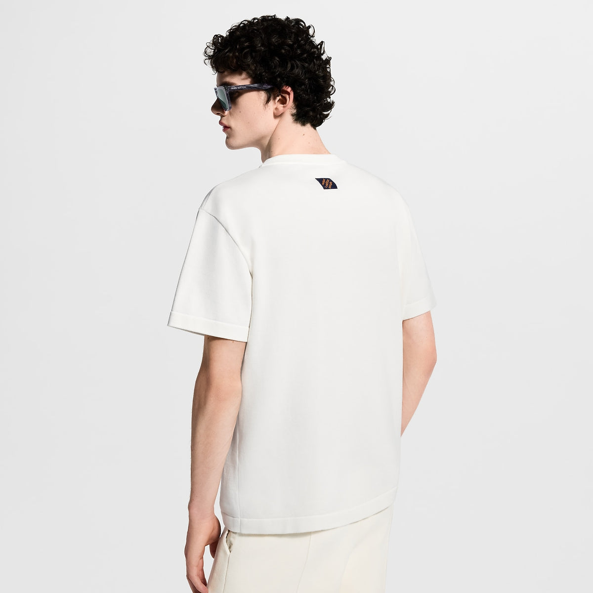tee-shirt blanc à manches courtes, orné d'un patch bleu roi représentant les mains de Pharrell Williams formant le geste LV, est le modèle Tee-shirt manches courtes et col rond à patch emblématique de Louis Vuitton.