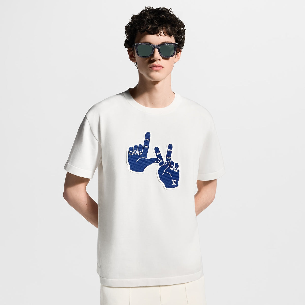 tee-shirt blanc à manches courtes, orné d'un patch bleu roi représentant les mains de Pharrell Williams formant le geste LV, est le modèle Tee-shirt manches courtes et col rond à patch emblématique de Louis Vuitton.